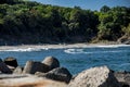 A close up of a rock next to a body of water. A beach with people and umbrellas in the distance Royalty Free Stock Photo