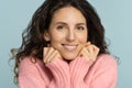 Woman keep hands under chin, looking at camera, smiling, wear rosy sweater, has no make up, isolated