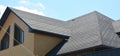 A close-up on a roof problem area covered with asphalt roof shingles and irregular shape window on the wall of the house