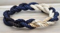 a close up of a rope bracelet on a wooden surface with a white and blue knot on it\'s end and a black Royalty Free Stock Photo