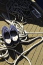 Close-up of a rope with a knotted end tied around a cleat on a wooden pier and shoes with anchors