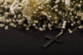 Close up of a rosary beads with a black cross in blurred white small flowers, black background Royalty Free Stock Photo