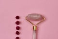 Close up of rose quartz facial massage roller and dried rose buds isolated over pink background Royalty Free Stock Photo