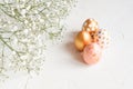 Close up of rose, white and golden decorated eeaster eggs with gypsophila on white concrete background. Copy space for text