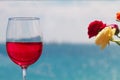 Close up of rose wine glass and a few flowers on background of defocused blue seaside view.
