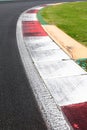 Rough curb at right turn on motor sport track with green field and black asphalt Royalty Free Stock Photo