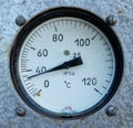 Close-up of a round analog temperature sensor mounted on a textured metal surface. Indicates temperatures from 0 to 120 degrees