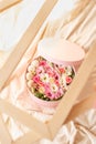 Close up of round pink box with ribbon,flowers,french macarons inside in wooden frames on the beige texture with open top