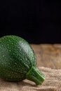 Close-up of a round zucchini lying on burlap cloth, rustic wooden board and black background