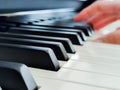 A close-up of a row of piano keys. In the blurred background, a pianist's hands can be seen practicing on the piano. Royalty Free Stock Photo