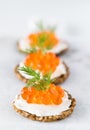 A close up of a row of rustic whole grain crackers topped with cream cheese and caviar and garnished with dill.