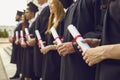 Graduate concept.Cropped image of row of students in black robes with diplomas in hands at graduation ceremony Royalty Free Stock Photo