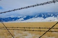 CLOSE UP: Rusty barbed wire fence runs around a pasture under the snowy Rockies