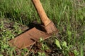 Close up of a rusty spade resting on a lawn in the garden. The earth is red. The handle is made of wood