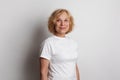 Close up of a 60s middle age woman smiling and wearing a white t-shirt on a white studio wall background Royalty Free Stock Photo
