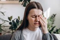 Close up of sad woman suffering from strong eye pain. Eyesight problem. Tired young brunette female touching eyes sitting on sofa Royalty Free Stock Photo