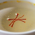 A close-up of saffron threads floating in a light yellow liquid, likely broth or tea. The Royalty Free Stock Photo