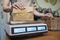 Close Up Of Sales Assistant In Sustainable Plastic Free Grocery Store Weighing Goods In Paper Bag On Digital Scales