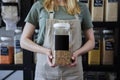 Close Up Of Sales Assistant In Sustainable Plastic Free Wholefood Store Holding Container With Blank Label