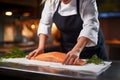 Close up salmon fillet and hand of chef woman in uniform.
