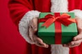 Close-up of Santa s hands presenting a green gift box with a red bow on a celebratory red Royalty Free Stock Photo