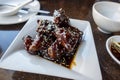 saucy baby back pork ribs on a white square plate inside an Asian restaurant