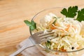 Close-up sauerkraut and fork in glass bowl is standing on light wooden table. Royalty Free Stock Photo