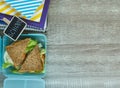 Close up School blue lunch box with homemade sandwich, green apple, cookies, on black chalkboard. Healthy eating at school.