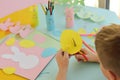 a close-up of a schoolboy who cuts an Easter card in the form of a rabbit out of colored paper with scissors. Easter