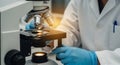 Close-up of a scientist in blue gloves using a microscope with illuminated specimen slide in a laboratory setting Royalty Free Stock Photo