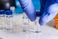 Close up scientist hand in rubber gloves takes a glass vial with a blue cap for HPLC analysis. Development of pharmaceuticals and