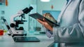Scientist in Lab Coat Analyzing Data on Tablet with Microscope and Laptop in Background Royalty Free Stock Photo