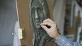 Close-up of Sculptor creating sculpture of human`s face on canvas while young woman posing to him in art studio Royalty Free Stock Photo