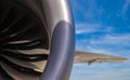 Close up section of jet engine with titanium blades and section of the wing on a blue sky background