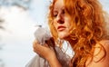 Close-up of a seductive young sexy redhead beautiful sensual woman portrait, ginger with long curly hair, looking at dragonfly