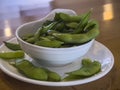 Close up, selective focus on edamame pods in a small white cup on a wooden table inside a restaurant Royalty Free Stock Photo