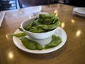 Close up, selective focus on edamame pods in a small white cup on a wooden table inside a restaurant Royalty Free Stock Photo