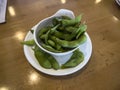 Close up, selective focus on edamame pods in a small white cup on a wooden table inside a restaurant Royalty Free Stock Photo