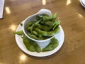 Close up, selective focus on edamame pods in a small white cup on a wooden table inside a restaurant Royalty Free Stock Photo