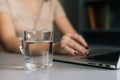 Close-up selective focus of glass water on table where unrecognizable business woman working on laptop computer at home Royalty Free Stock Photo