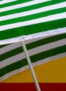 Close up and selective focus at green and white striped beach umbrella laying on red and yellow wall in vertical frame Royalty Free Stock Photo