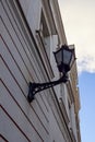 Close up, selective focus of old-style black street lamp lantern hanging on the renewed striped building wall. Blue sky Royalty Free Stock Photo