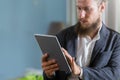 Close up selective focus at tablet in hand of businessman. Handsome businessman with beautiful bearded standing working online Royalty Free Stock Photo