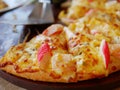 Selective focus of well-done fresh appetizing crab stick, ham, cheese pizza being served on a wooden tray