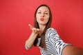 Close up selfie shot of pretty young woman in casual striped clothes blowing kisses send air kiss isolated on bright red Royalty Free Stock Photo