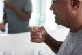 Close Up Of Senior Man In Bathroom Mirror Wearing Pajamas Taking Vitamin Supplement Tablet