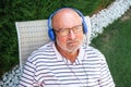 Close-up of a retired man with a thoughtful face wearing blue headphones sitting on a lawn chair Royalty Free Stock Photo