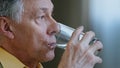 Close up senior old mature Caucasian man looking away thinking holding glass of clean still water drinks h2o health care