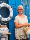 Close up of senior pretty lady with gray hair looking at camera. Romantic and rustic corner with blue door. Navy style accessories