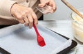 Close-up of a senior woman hands while greasing a baking tin using a red silicone brush